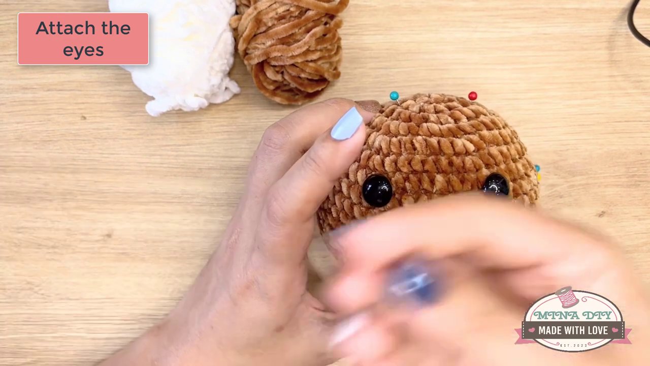 Bringing Your Amigurumi to Life: A Step-by-Step Guide to Embroidering Eyes and Noses 4 A needle is shown sewing a small, dark nose piece onto the animal's face, with text indicating the placement between specific rounds.